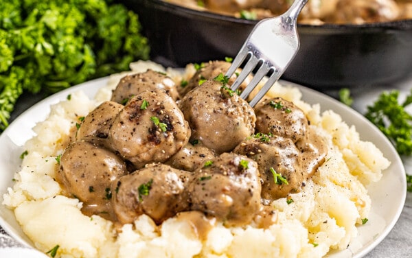 A fork poking into a Swedish meatball on a plate of mashed potatoes.