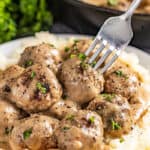 A fork poked into Swedish meatballs and gravy.