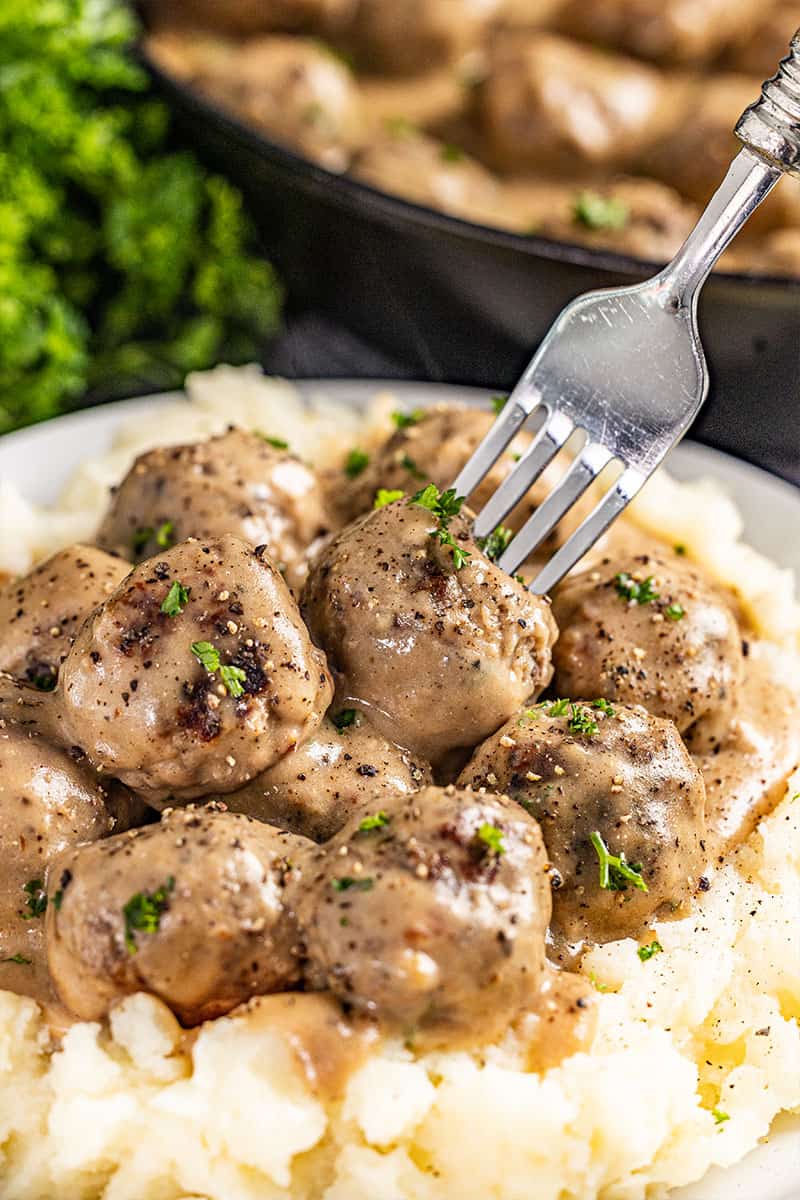 A fork poked into Swedish meatballs and gravy.