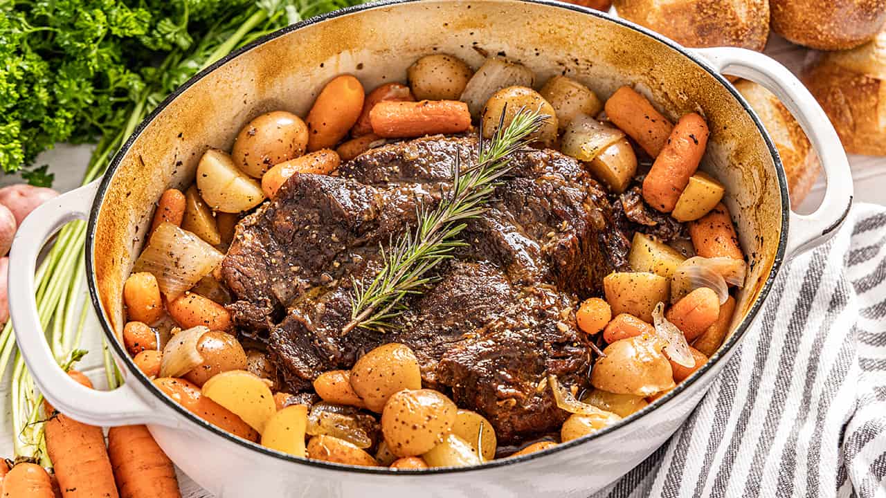Pot roast surrounded by potatoes and carrots in a large pot.