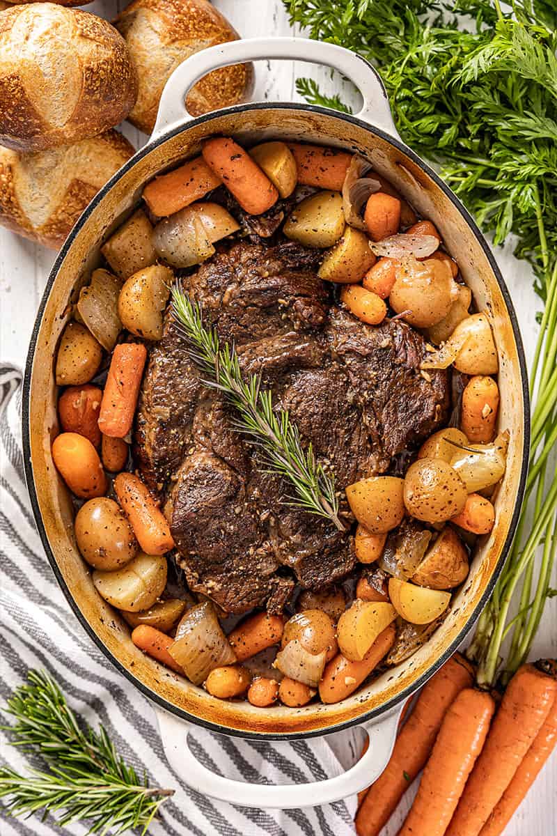 Overhead view of a large pot roast in an enameled cast iron pot surrounded by potatoes, carrots, and onions.