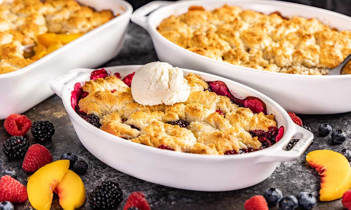 Berry cobbler in a small white baking dish with ice cream on top.