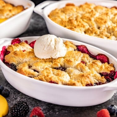 Berry cobbler in a small white baking dish with ice cream on top.