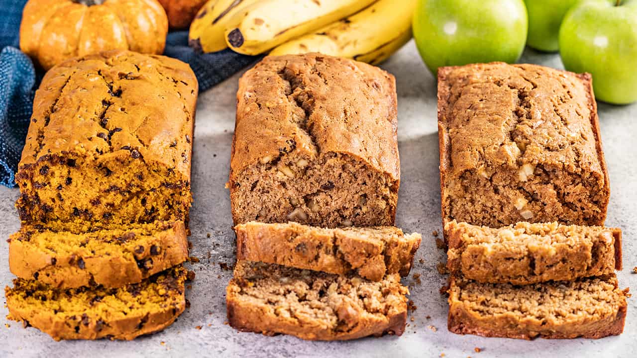 Pumpkin, apple, and banana quick bread loaves with slices cut.