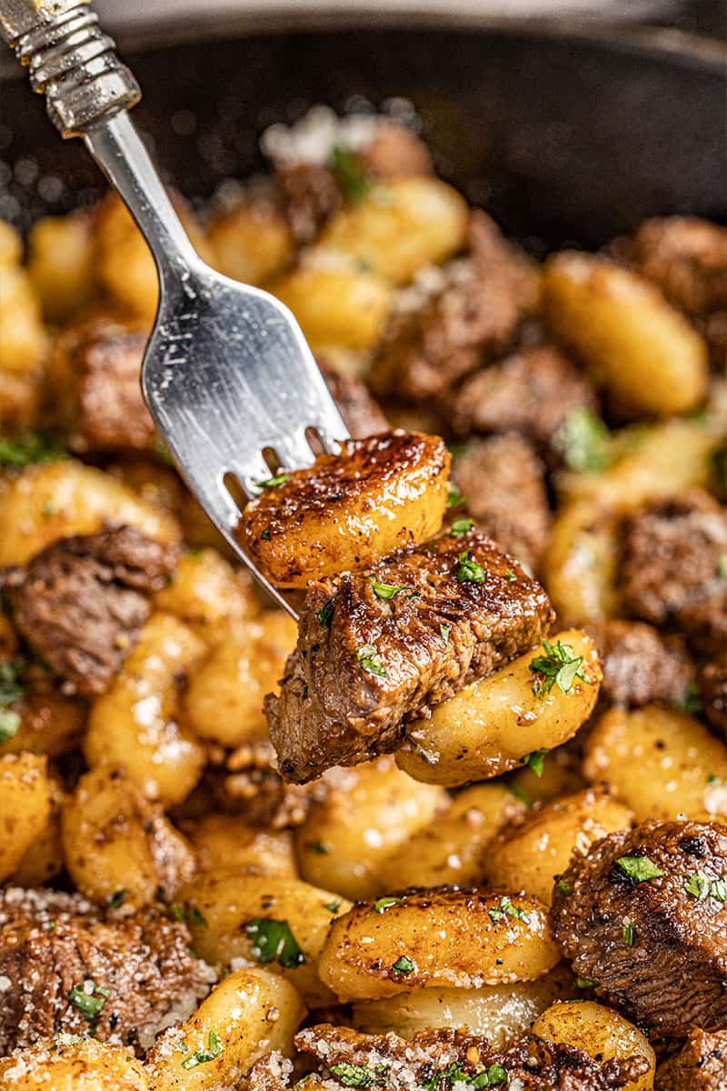 A fork filled with gnocchi and steak bites.