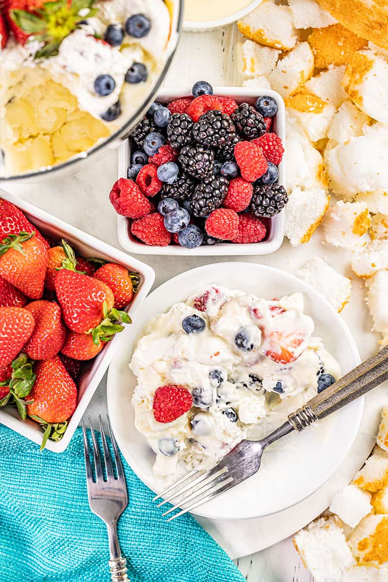 Overhead view of a serving of creamy berry trifle on a dessert plate and baskets of berries nearby.