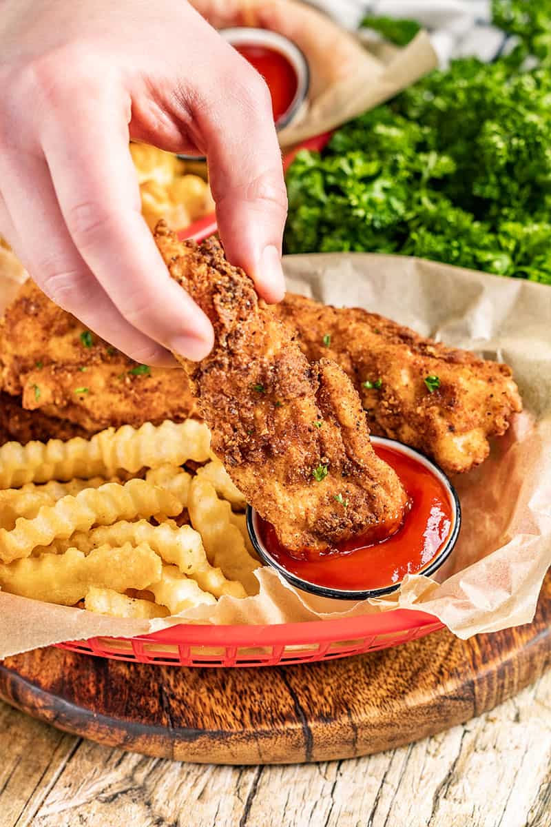 A hand dunking a homemade chicken finger into ketchup.