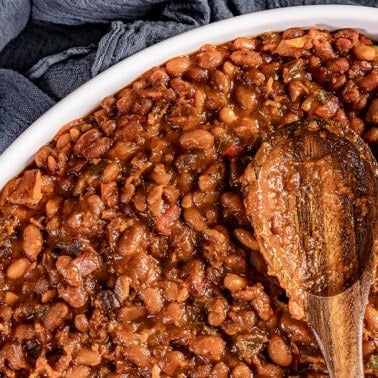 Overhead view of homemade baked beans with a wooden spoon.