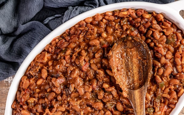 Overhead view of homemade baked beans with a wooden spoon.