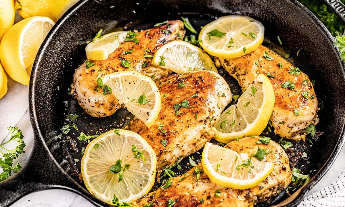 Looking into a cast iron skillet filled with lemon slices and cooked chicken breasts.