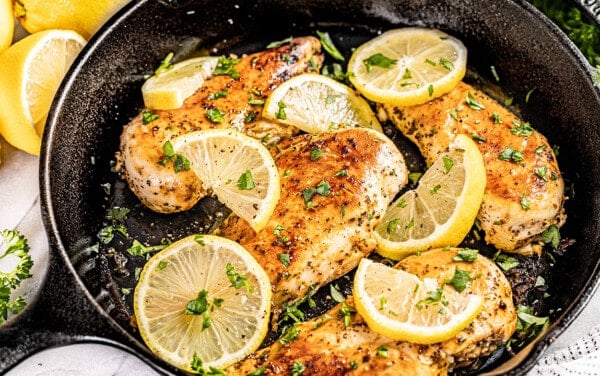 Looking into a cast iron skillet filled with lemon slices and cooked chicken breasts.