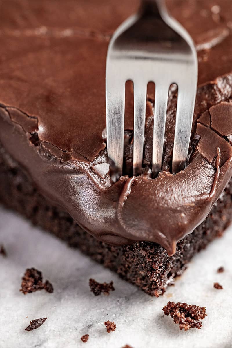 A fork sticking into a chocolate cake with cooked chocolate fudge icing.