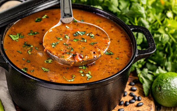 A ladle filled with homemade black bean soup in a large pot.