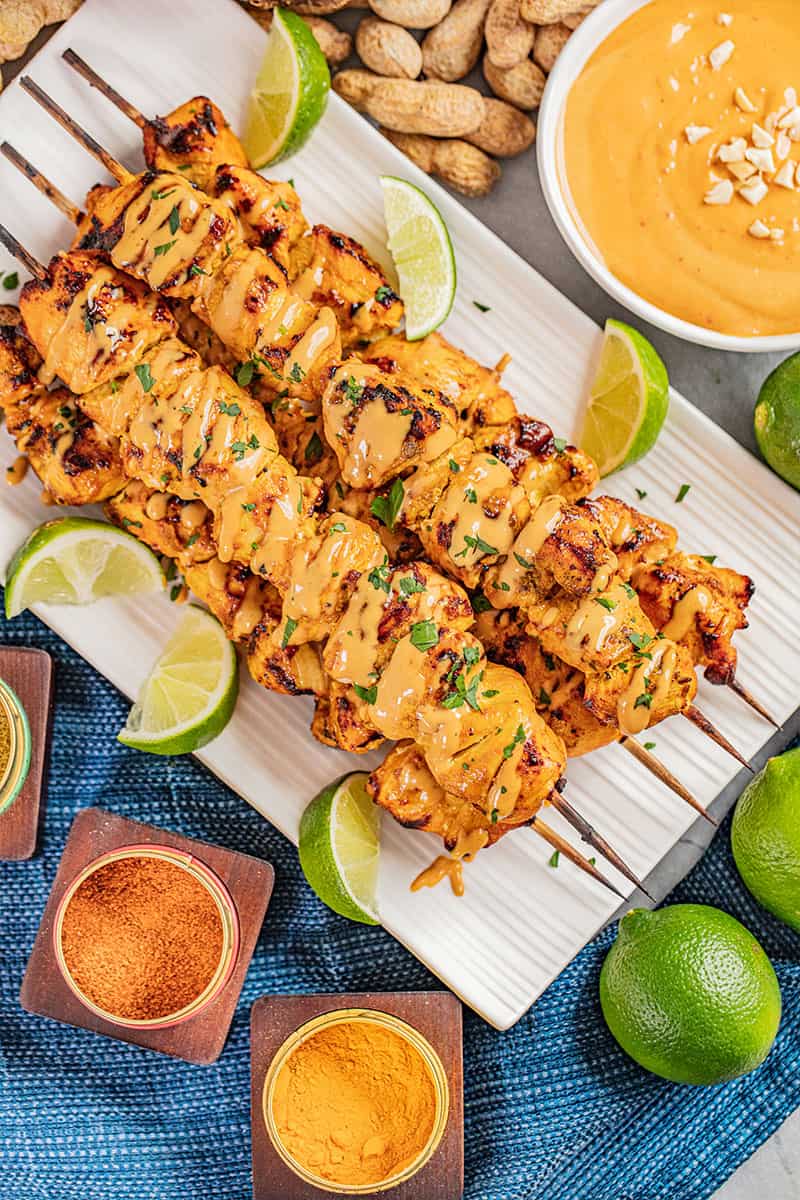 Overhead view of chicken satay on skewers with peanut sauce.