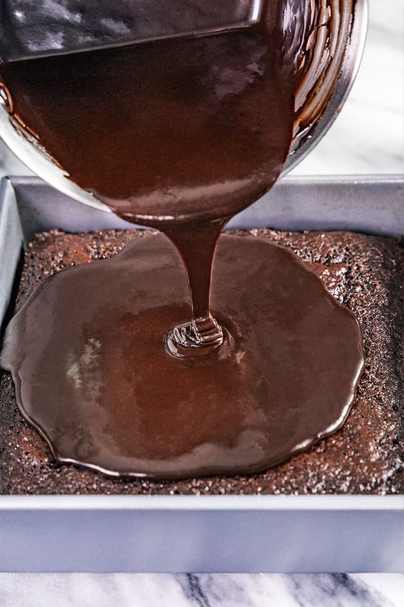 Fudge icing being poured onto a chocolate cake. 
