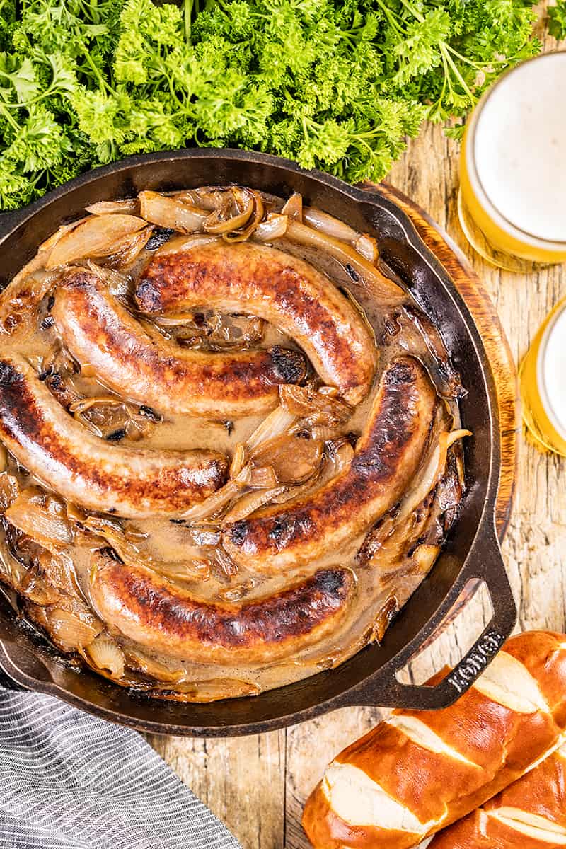Overhead view of bratwurst and onions in a cast iron skillet.