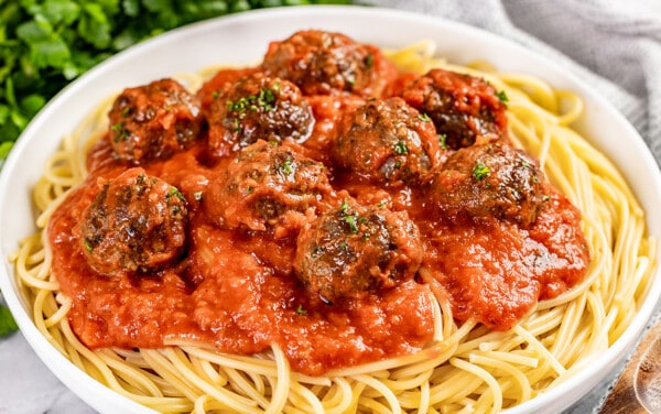 Close up view of baked meatballs on top of spaghetti.