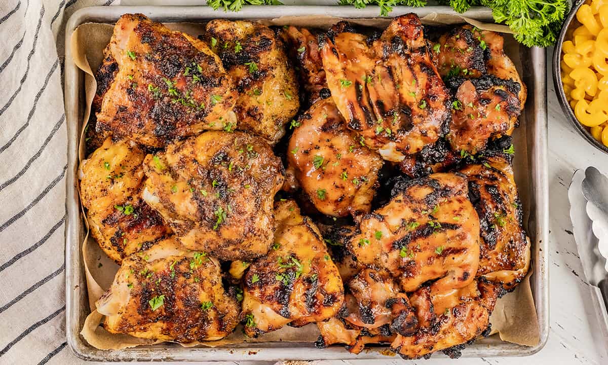 Overhead view of grilled chicken thighs on a baking sheet.