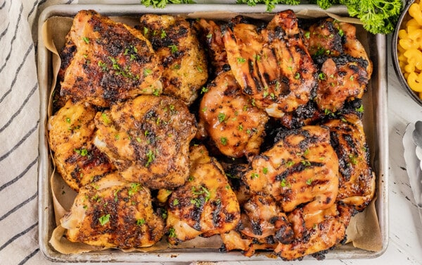 Overhead view of grilled chicken thighs on a baking sheet.