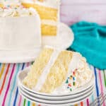 A piece of vanilla cake on a plate with the rest of the cake in the background.