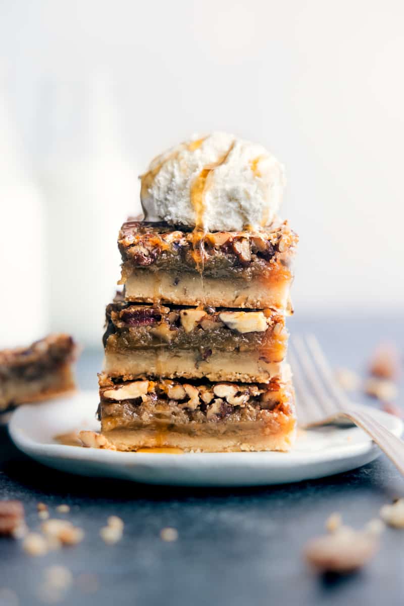 Stack of three pecan bars on a white plate topped with vanilla ice cream and a drizzle of caramel syrup.