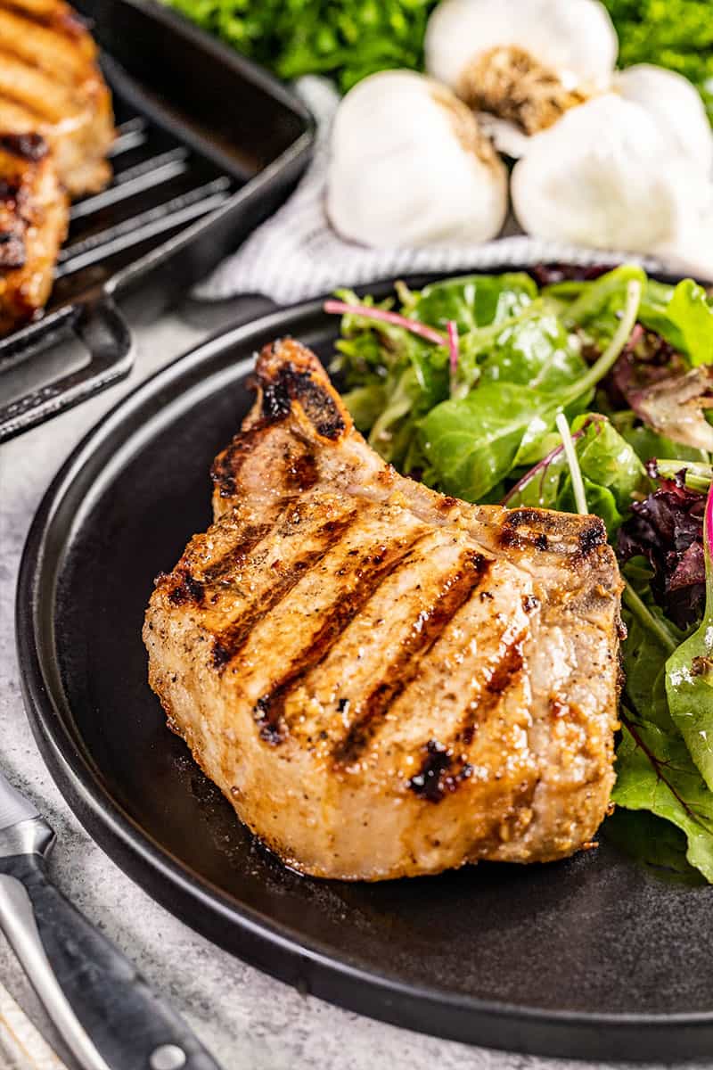 Close up view of a pork chop on a plate with a salad.