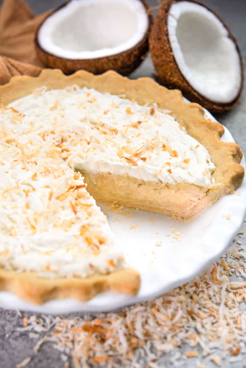 A whole coconut cream pie on a pie plate with one slice removed.