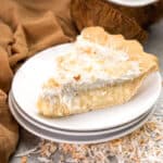 A slice of coconut cream pie on a stack of dessert plates.