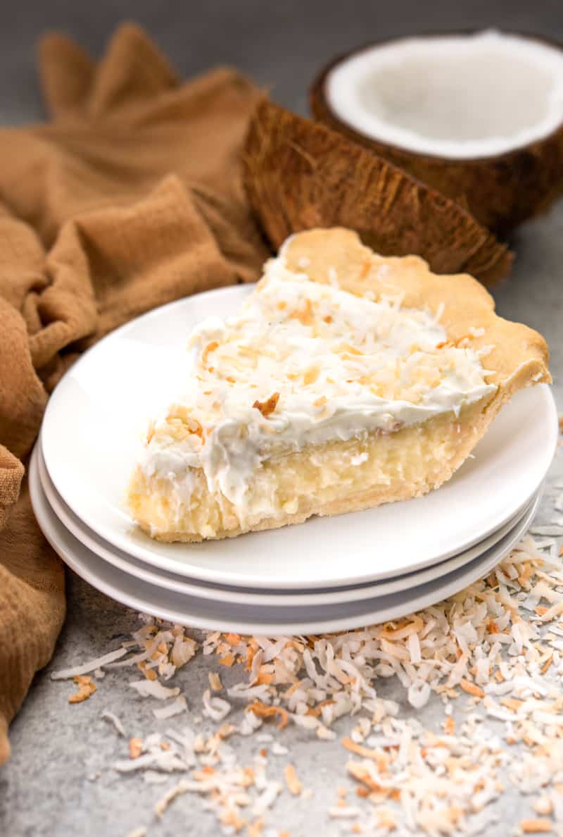 A slice of coconut cream pie on a stack of dessert plates.