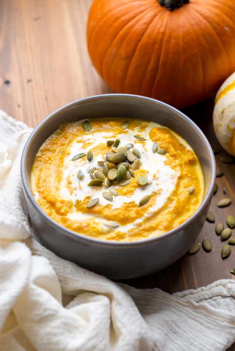 A bowl of creamy pumpkin soup with pumpkin seeds on top.