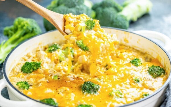 A wooden spoon filled with creamy chicken broccoli casserole being held over the baking dish.