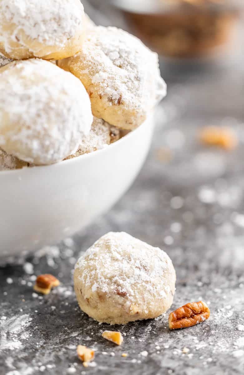 A pecan sandy sitting next to a bowl filled with pecan sandies.