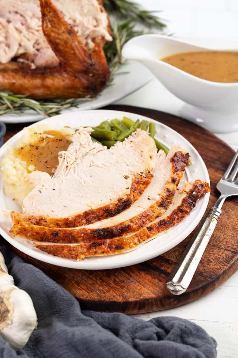 Sliced Thanksgiving turkey on a plate with mashed potatoes and gravy.