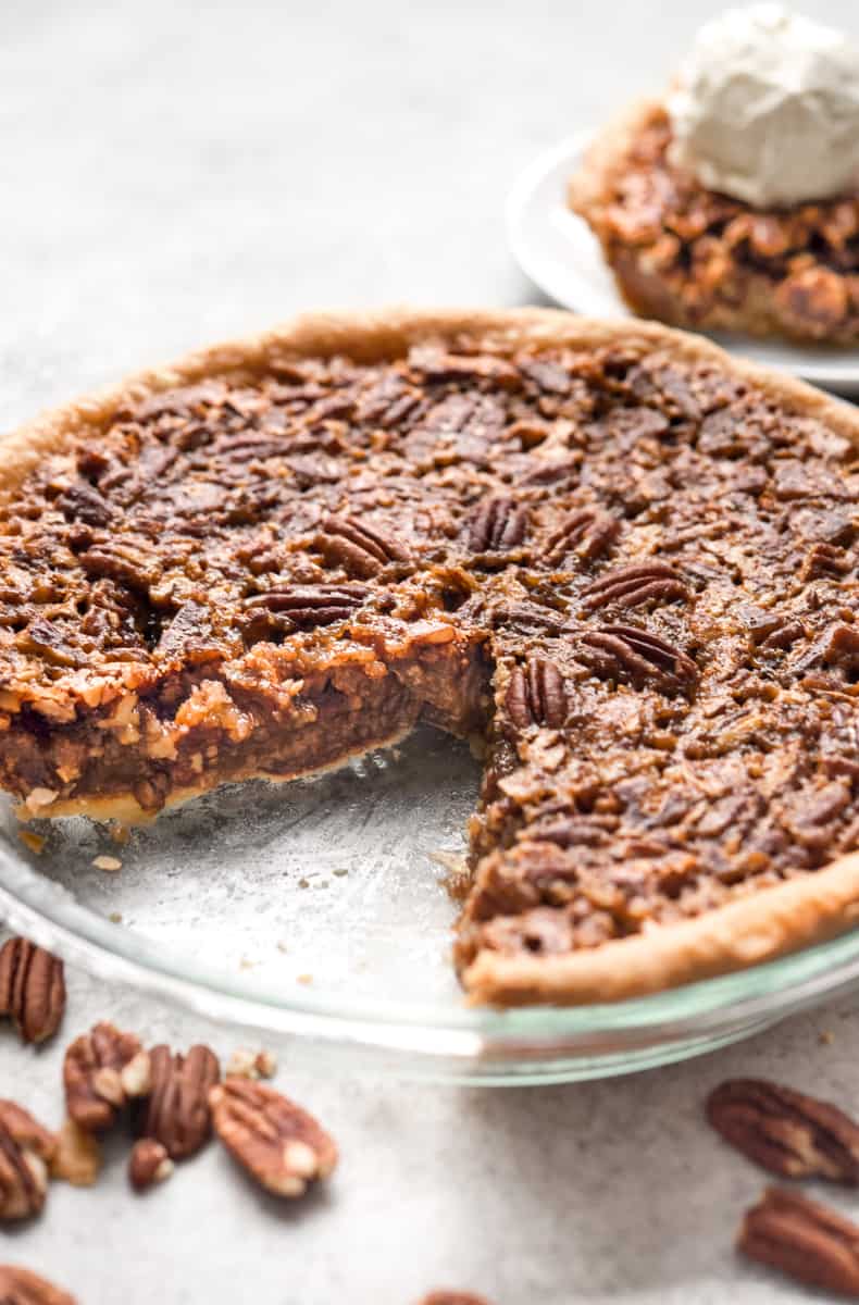 A whole pecan pie in a pie plate with a slice removed.