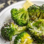 Broccoli cooked in an air fryer on a white dinner plate.