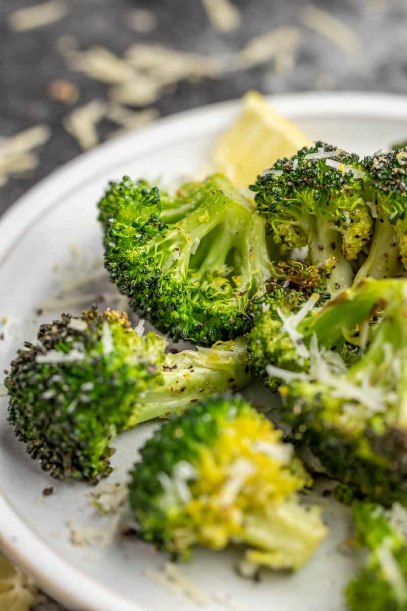 Broccoli cooked in an air fryer on a white dinner plate.