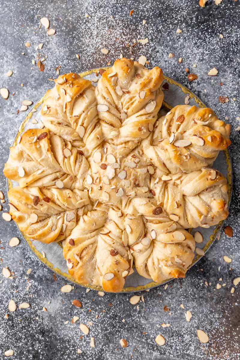 Overhead view of a loaf of Almond Star Bread surrounded by loosely scattered slivered almonds.