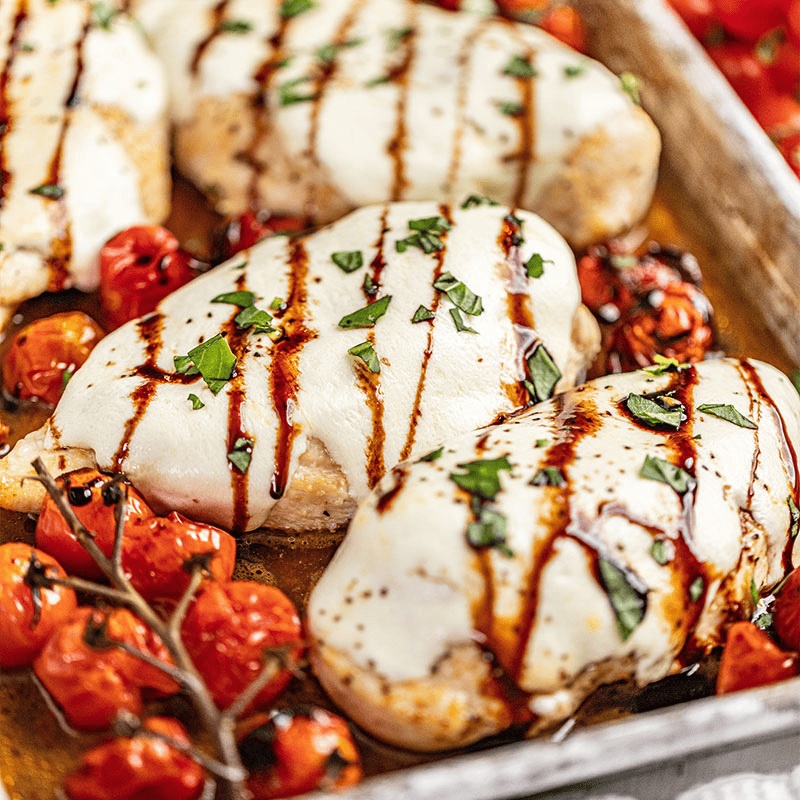 Chicken Caprese on a sheet pan surrounded by bursting roasted tomatoes.