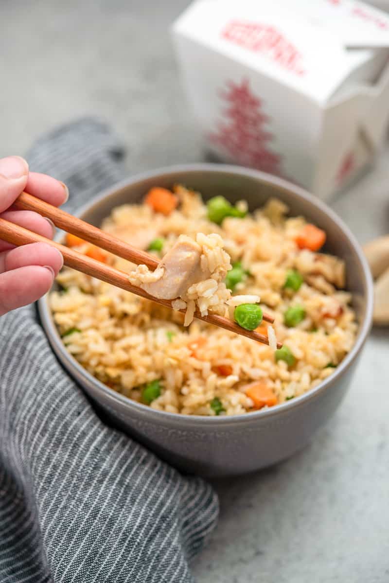 A hand holding chopsticks scooping out some chicken fried rice from a bowl.