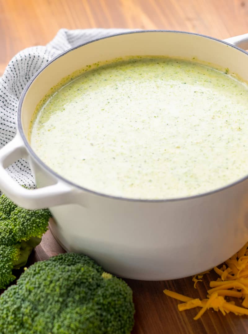 A white enameled cast iron pot filled with cream of broccoli soup.