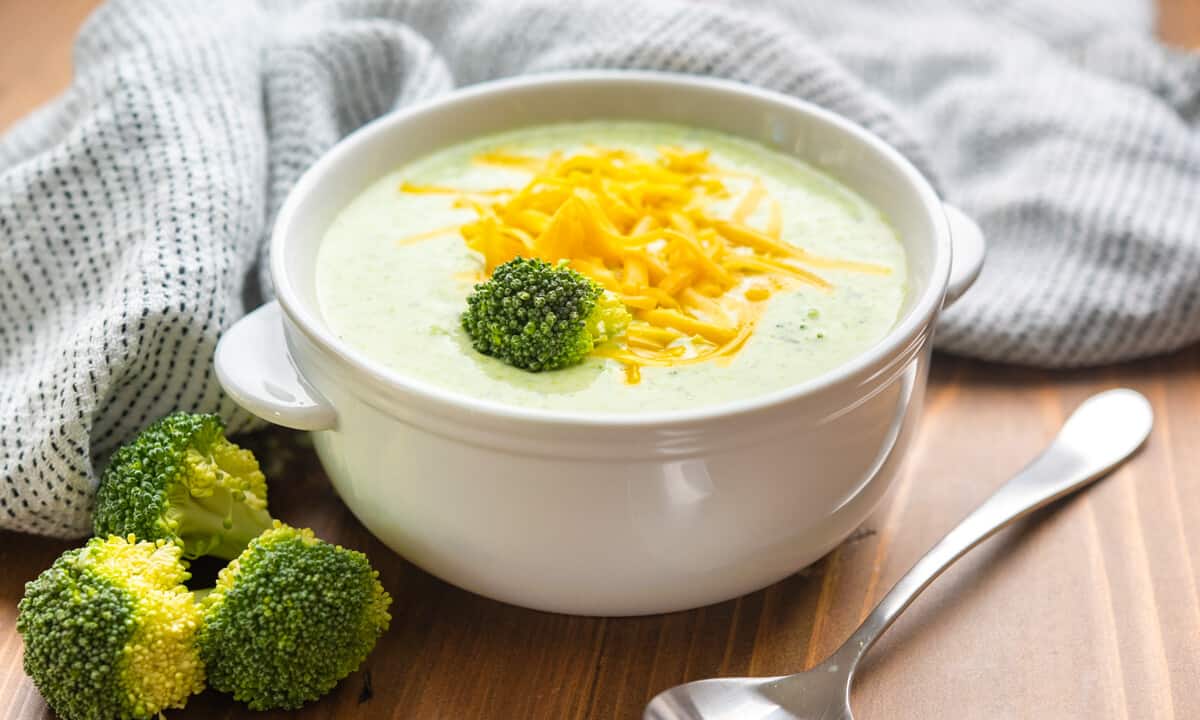 A bowl of cream of broccoli soup topped with shredded cheddar cheese.