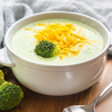 A bowl of cream of broccoli soup topped with shredded cheddar cheese.