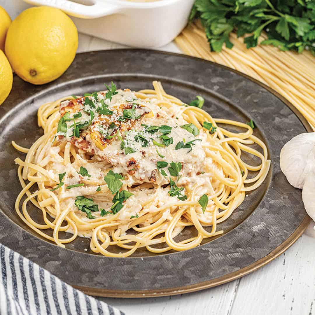 Chicken francese served over a bed of linguine on a metal plate.