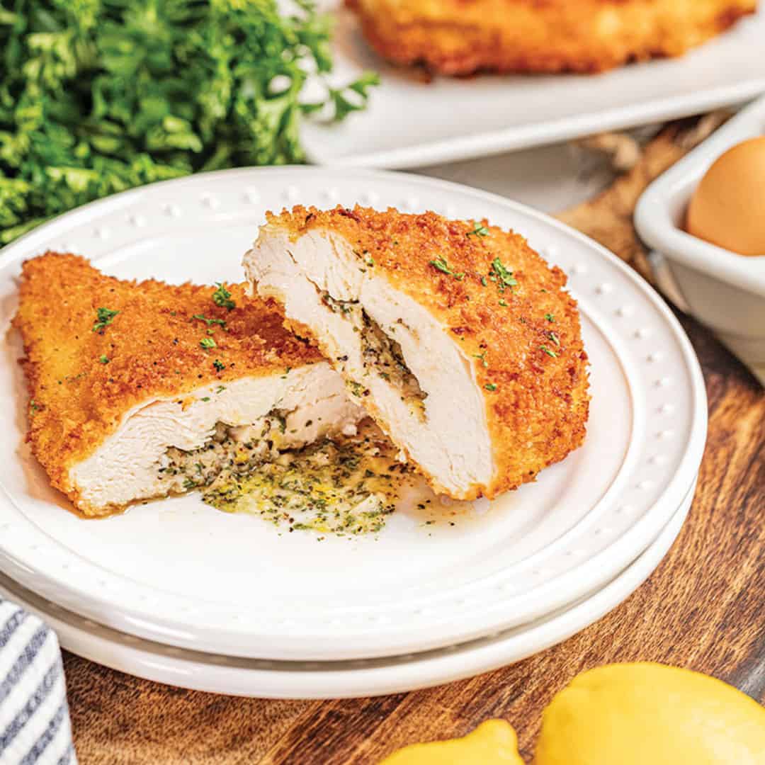 Chicken kiev sliced in half on a white plate with the buttery filling spilling out.