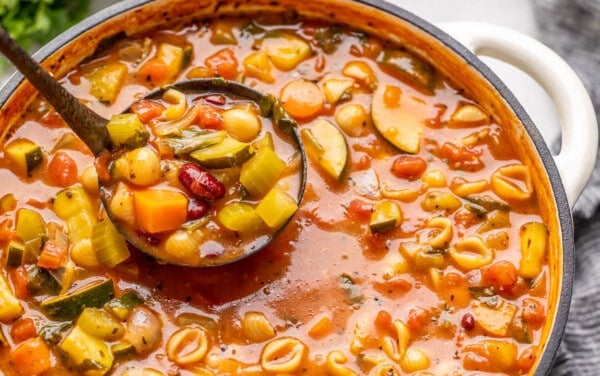 A ladle full of minestrone soup being scooped out of a soup pot.