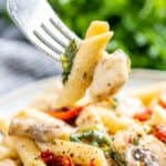 A fork holding up a bite of Italian chicken and pasta.