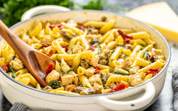 A wooden spoon resting in a pot of Italian chicken and pasta.