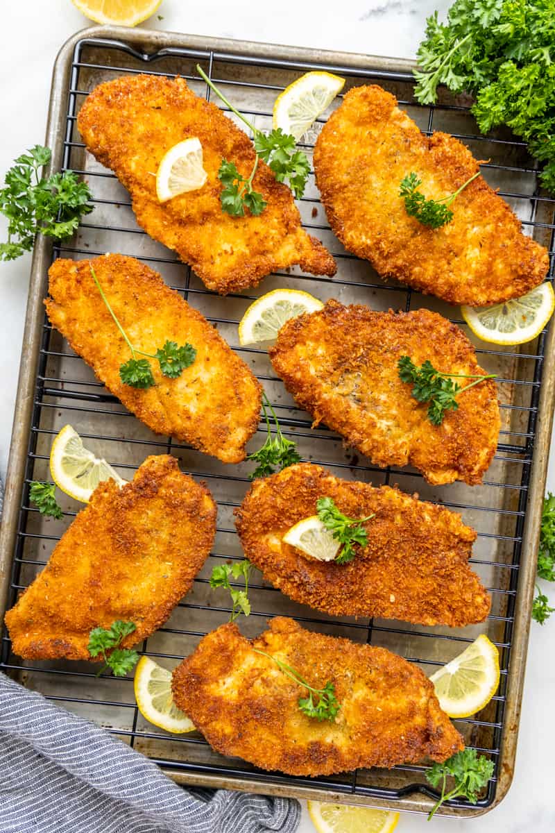 An overhead view of chicken cutlets on a cooling rack.