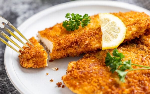 A fork poking into a chicken cutlet on a plate.