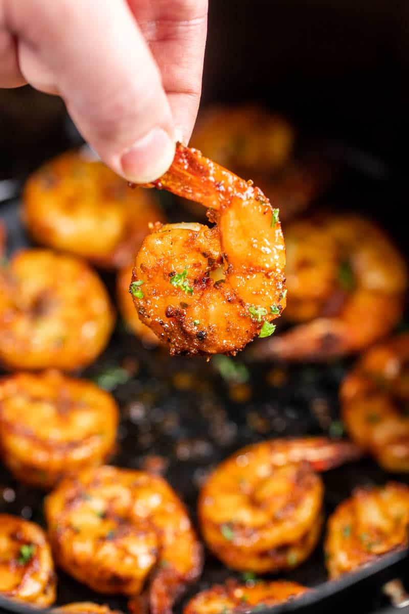 A hand holding a piece of air fryer shrimp by the tail.